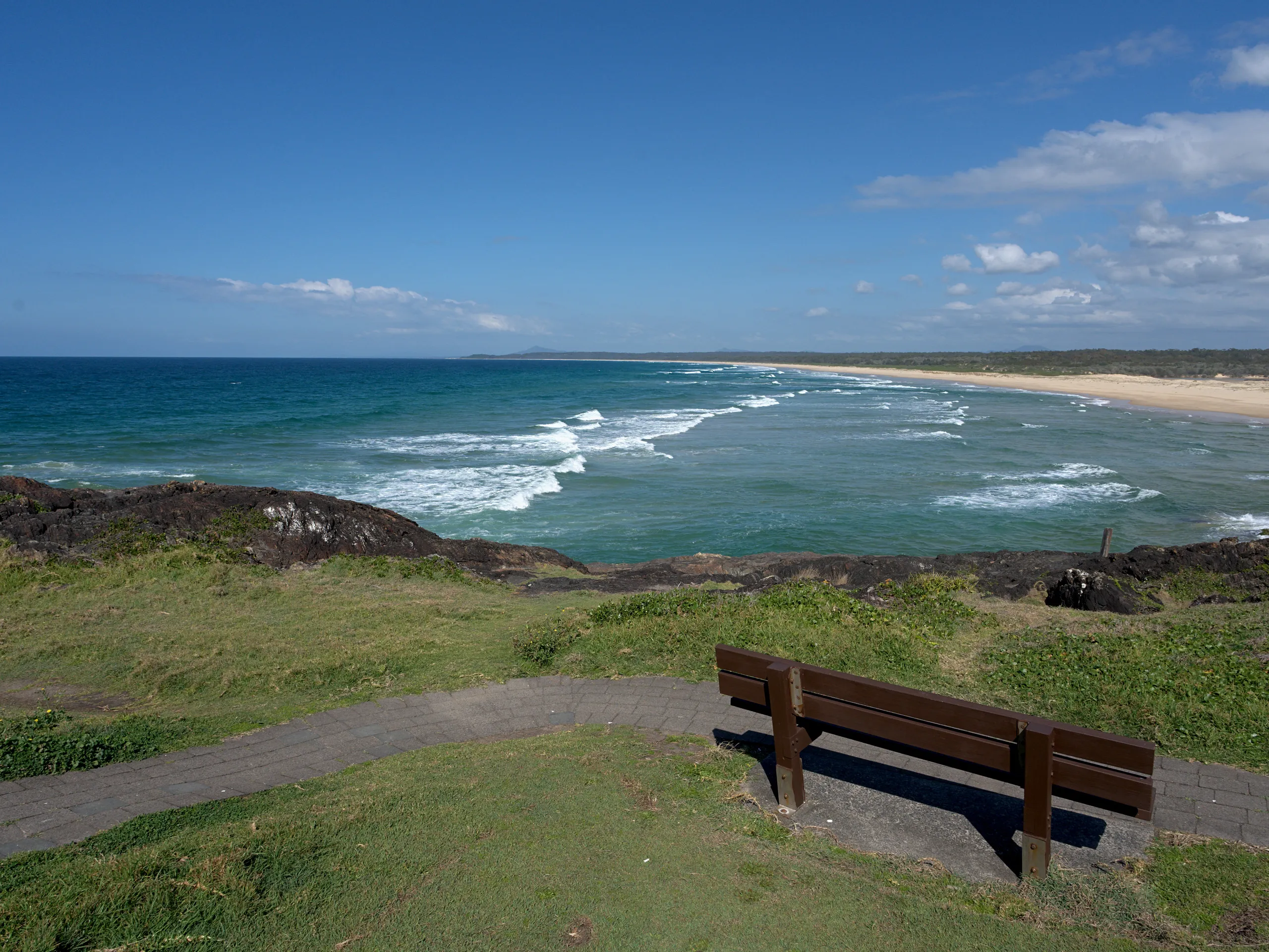 A bench on Bonville Headland looking south along the empty sand of Bonville Beach